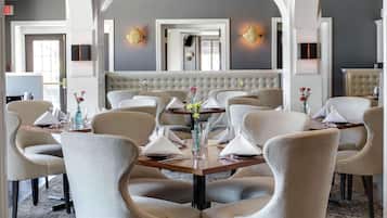 A dining area with a round table, upholstered chairs, a chandelier, and a tufted bench in the background.