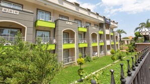 A multi-story hotel with balconies, a well-maintained lawn, and a statue in the foreground. - Rich Melissa Hotel (Kemer)