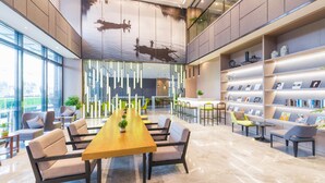 A modern lobby with a long wooden table, comfortable seating, a large window, and a wall with framed pictures. - Atour Hotel International Tourist Resort Xiuyan Road Shanghai (Shanghai)
