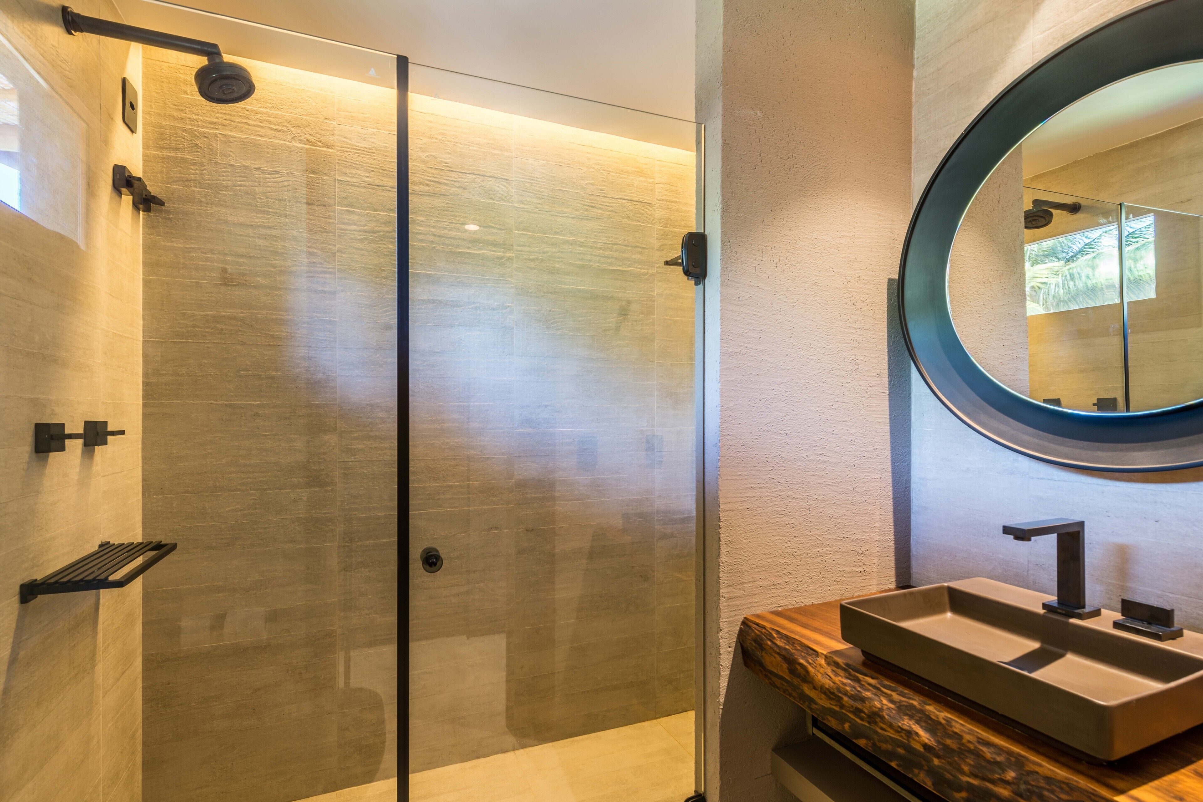 A modern bathroom with a glass-enclosed shower, a wooden vanity, and a round mirror.