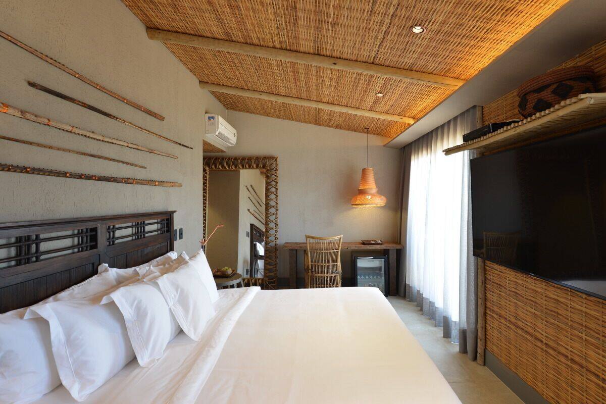 A hotel room with a large bed, a desk with a chair, a TV, and a ceiling with a woven design.