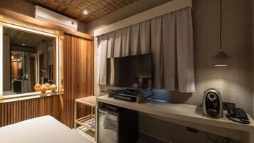 A modern hotel room with a large flat-screen TV, a minibar, a desk with a telephone, and a mirror.