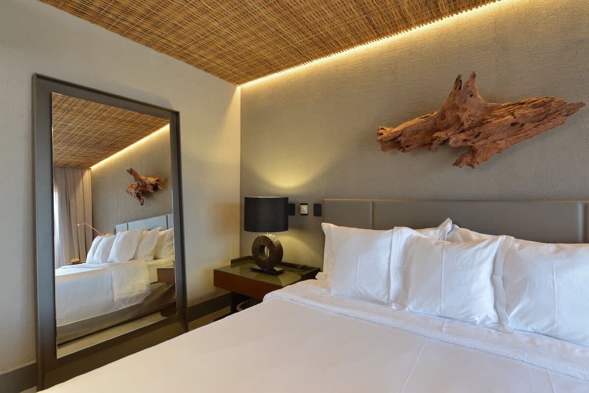 A hotel room with a large bed, a nightstand with a lamp, a mirror, and a wooden wall decor.