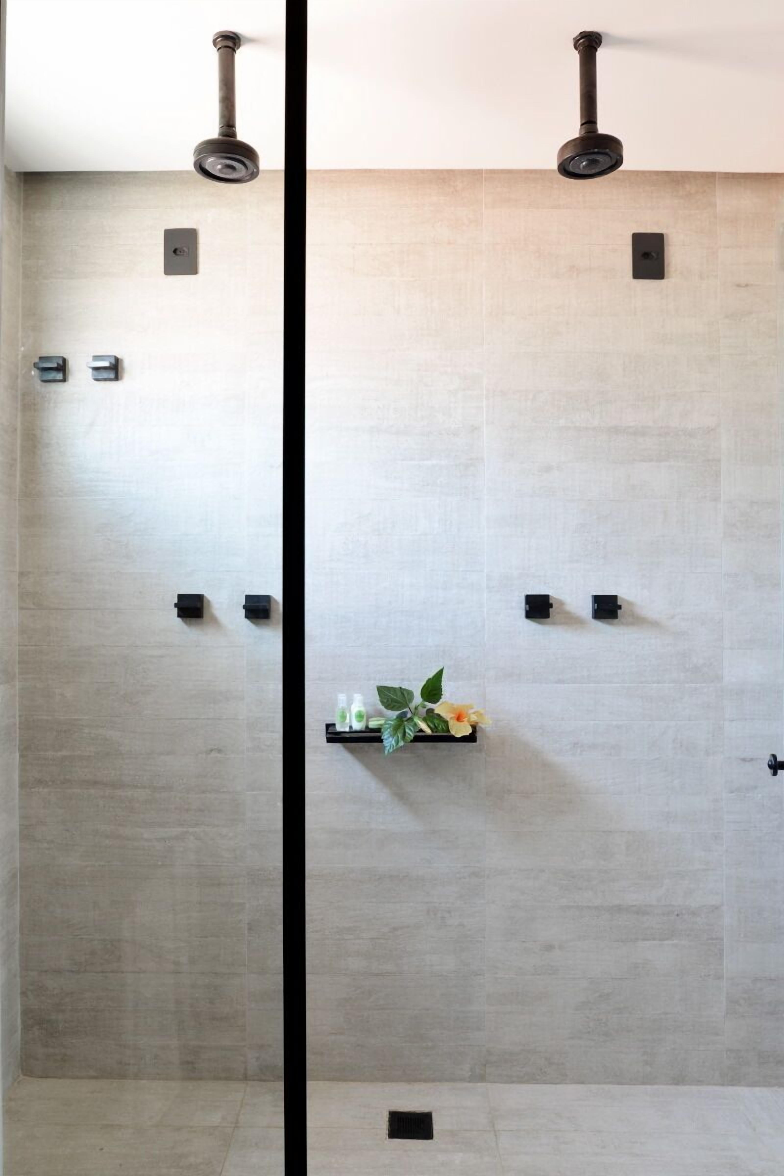 A modern bathroom with a large mirror, a shower area, and a shelf with toiletries.