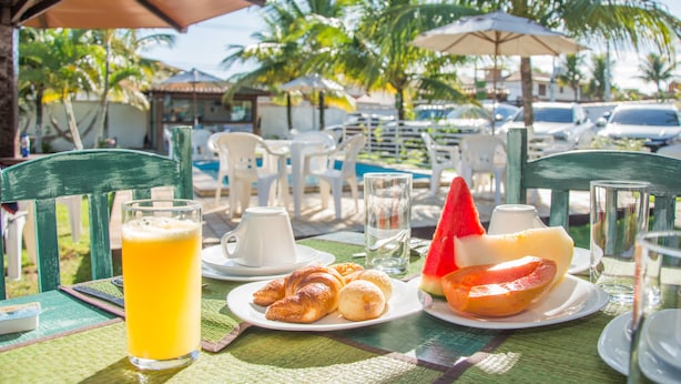 Una mesa dispuesta para el desayuno con croissants, un vaso de jugo de naranja y un plato con una tajada de sandía.
