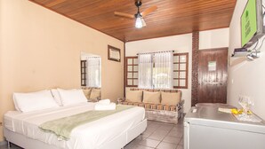 Una habitación de hotel con una cama, un sofá, una pequeña mesa con un vaso y un ventilador de techo.