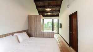 A bedroom with a large bed, wooden paneling, a bench, and a view through a glass door. - Penghu Bay Resort (Magong)