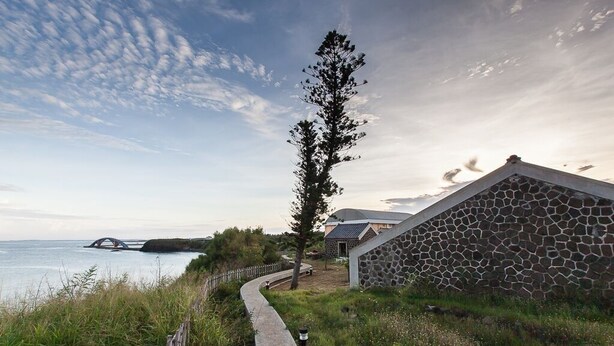 A coastal property with a stone wall, a pathway, and a view of the sea and a bridge in the distance. - Penghu Bay Resort (Magong)