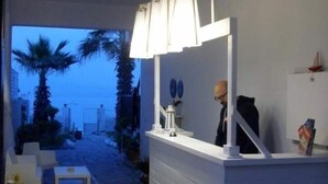 Un espace d’accueil moderne et minimaliste, avec un sol carrelé en pierre, des meubles blancs et une vue sur la mer en arrière-plan.