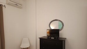 Une chambre à coucher comprenant un lit, une table de chevet avec un téléviseur à écran plat, une commode, une chaise et un miroir fixé au mur.