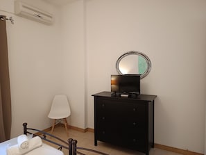 Een slaapkamer met een bed, een nachtkastje met een flatscreen televisie, een kast, een stoel en een spiegel aan de muur.
