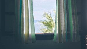 Une fenêtre avec des rideaux légers, une vue sur la mer et un palmier.