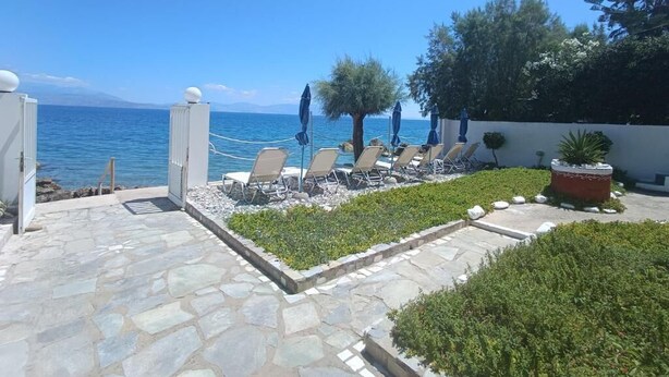 Une terrasse en pierre avec des chaises longues et des parasols, donnant sur une étendue d’eau.
