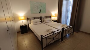 A double bed with white linens and two bedside tables with lamps, a painting on the wall, and a window with curtains. - Villa Constantina Apartments (Xylokastro-Evrostina)