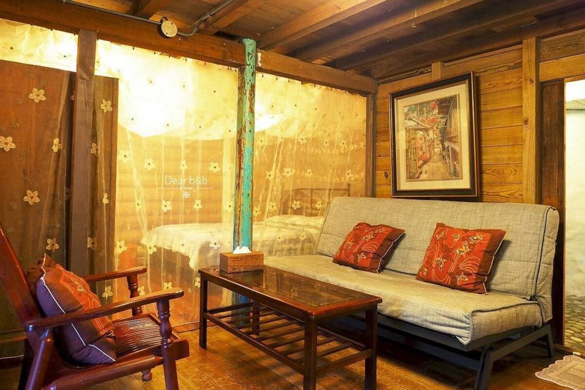 A cozy room with a wooden ceiling, a sofa with patterned cushions, a wooden chair, and a table with a tissue box.
