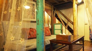 A rustic room with a wooden staircase, a bed with patterned bedding, and a table with a box on it. - Qi Tang Lane (New Taipei City)