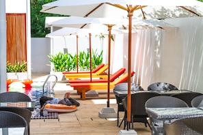 An outdoor patio area with wicker furniture, umbrellas, and a pool. - Sleep Pod Hostel (Siem Reap)