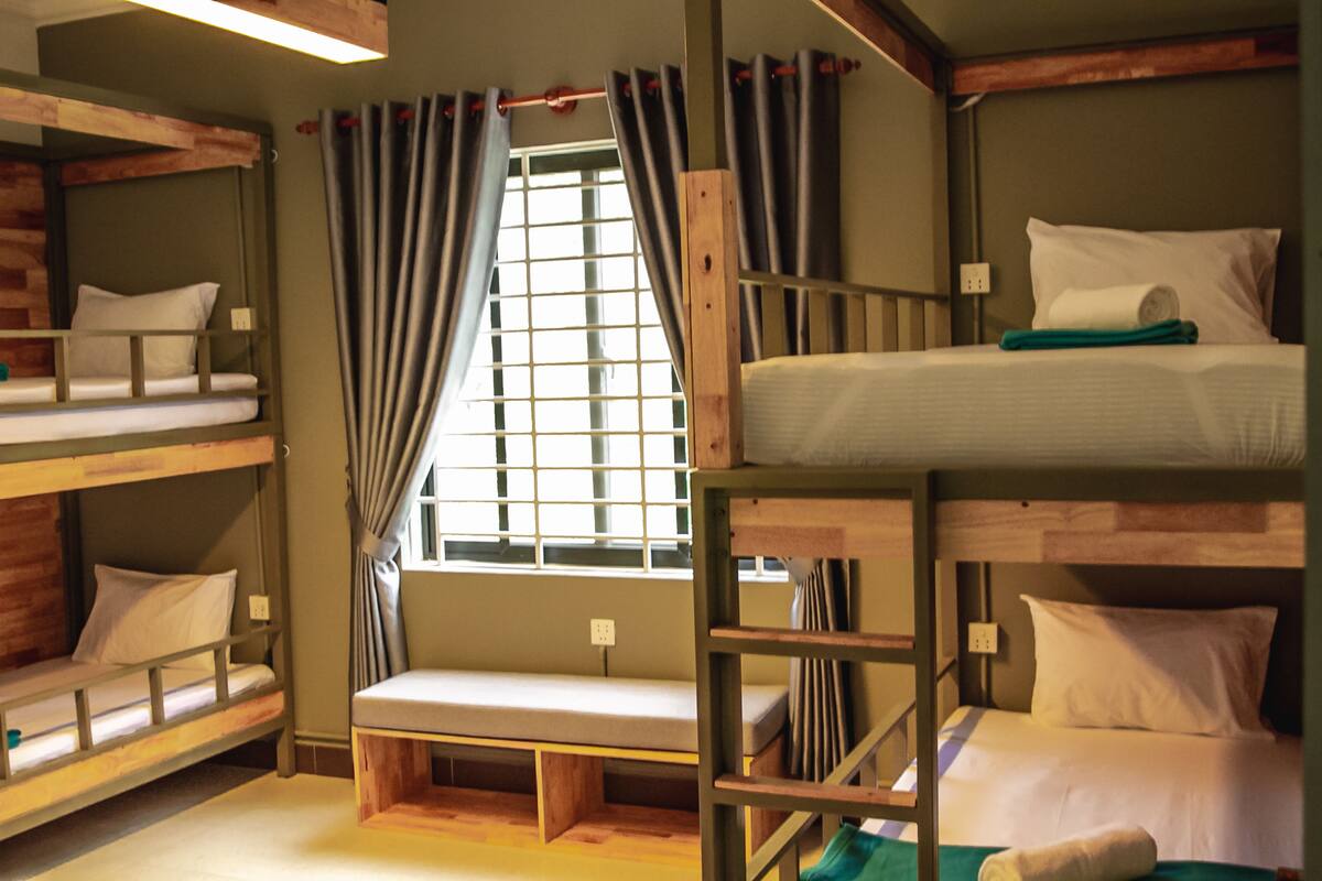 Une chambre avec un lit superposé, une fenêtre, des rideaux et un banc.