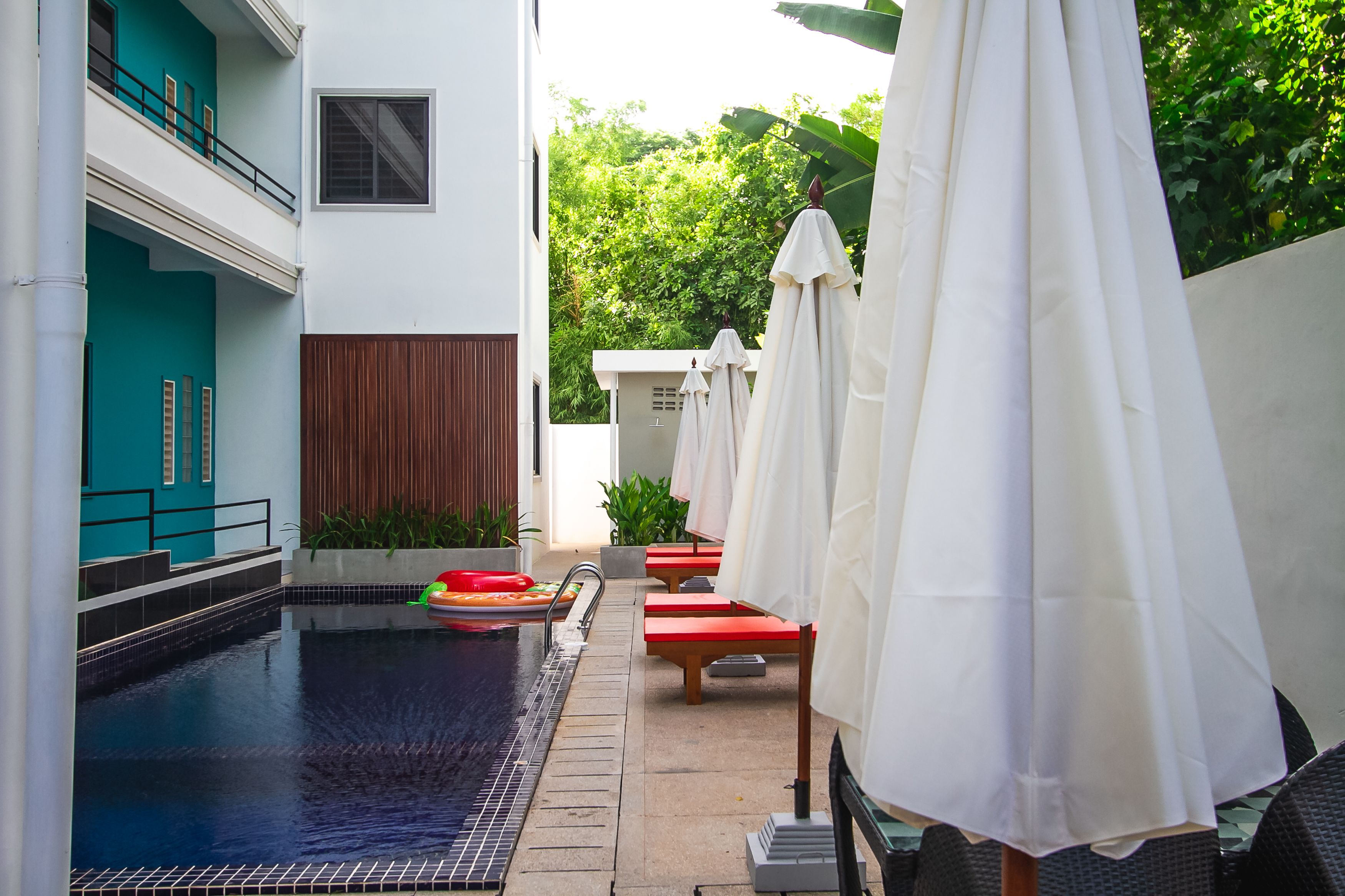 A swimming pool with a tiled deck, red lounge chairs, and white umbrellas.