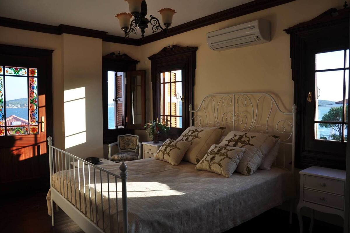 Ein Schlafzimmer mit Bett, Sessel, Nachttisch, Fenster mit Aussicht und Klimaanlage.