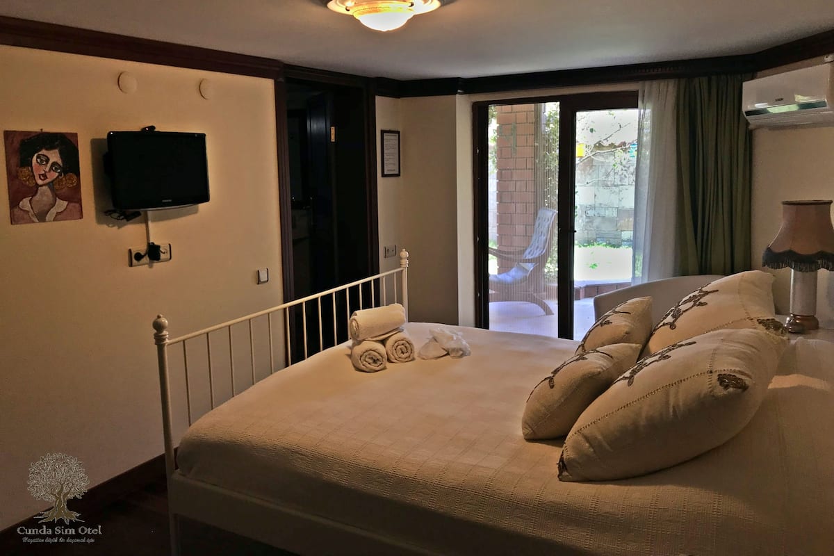 Ein Schlafzimmer mit Bett, einem an der Wand montierten Fernseher und Blick durch eine Glastür nach draußen.
