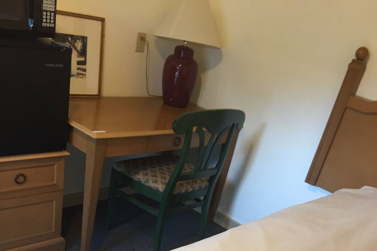 A hotel room with a bed, a desk, a chair, a lamp, and a television.