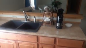 A kitchen with a double sink, a coffee maker, and a basket with utensils. - Mt. Baker Hotel (Concrete)