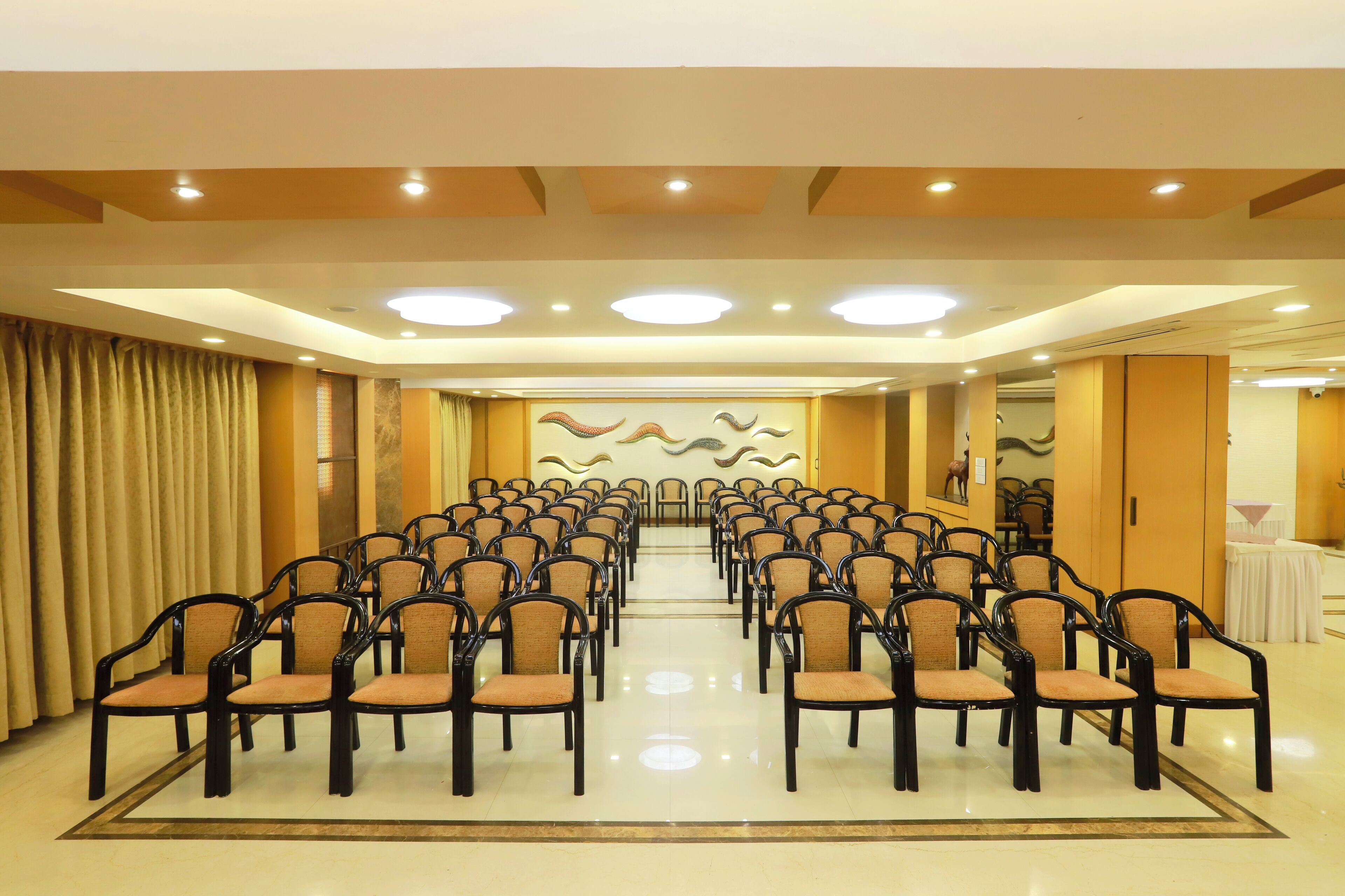 Un salón de conferencias con filas de sillas orientadas hacia un escenario, una araña de cristal y una pared decorativa.