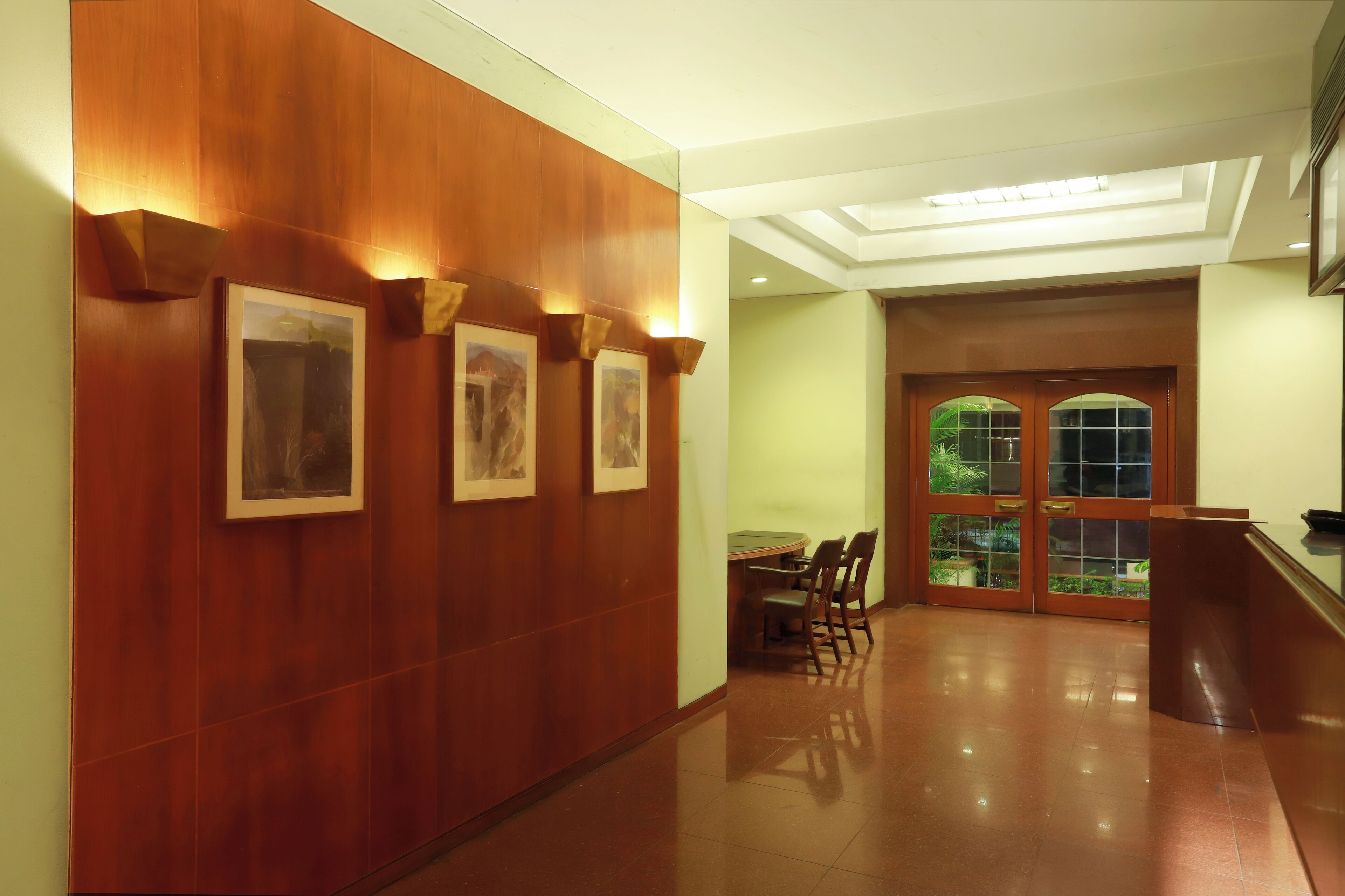 Un couloir aux murs recouverts de lambris en bois, orné de tableaux encadrés, avec une table ronde entourée de chaises et une porte vitrée donnant sur l’extérieur.