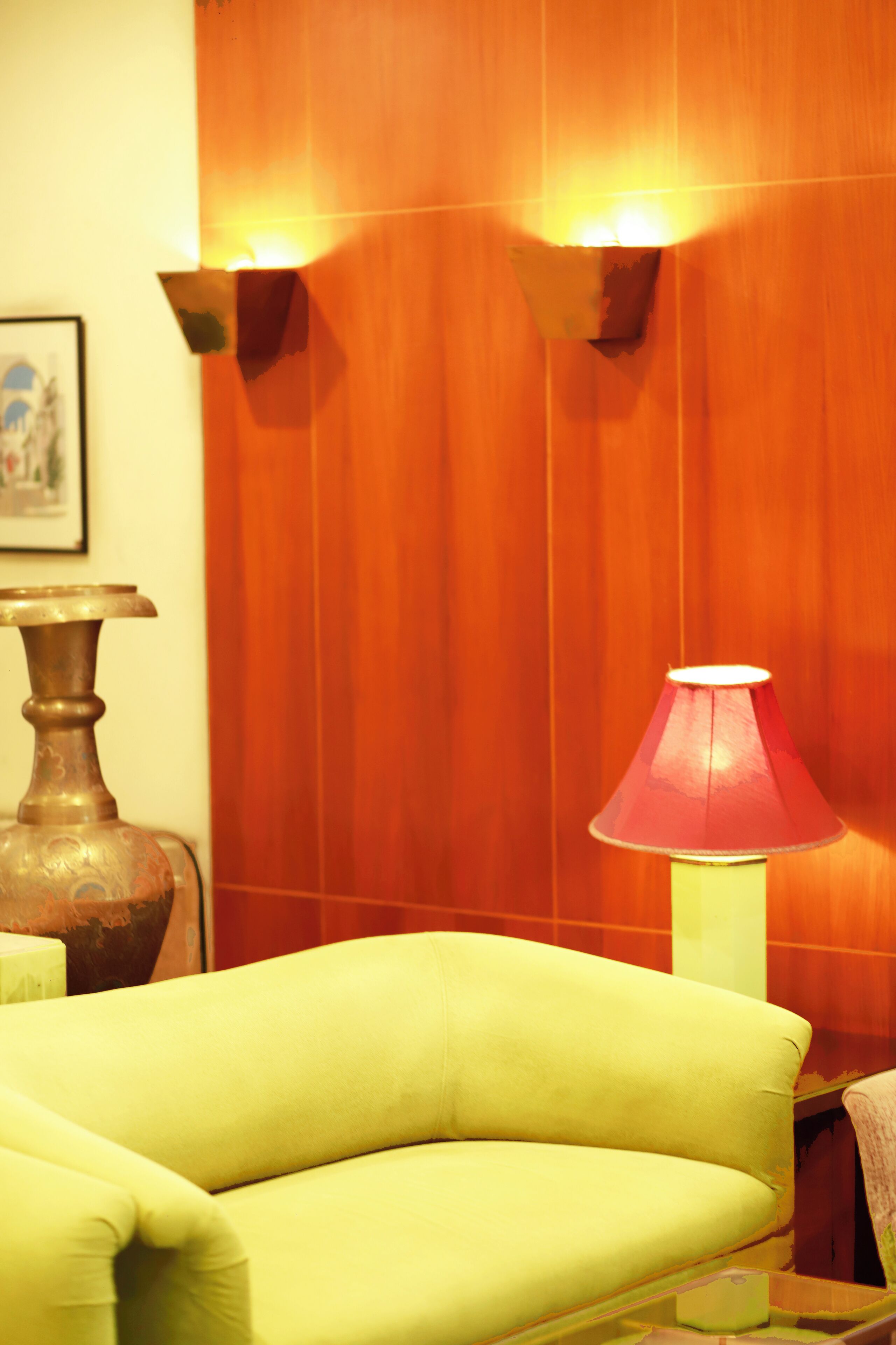 A room with a green sofa, a red lamp, and a wooden wall with two wall sconces.