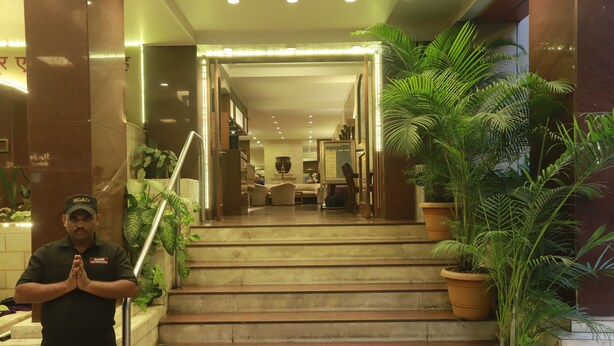 A hotel entrance with a security guard, a staircase, and potted plants. - Kohinoor Executive (Pune)