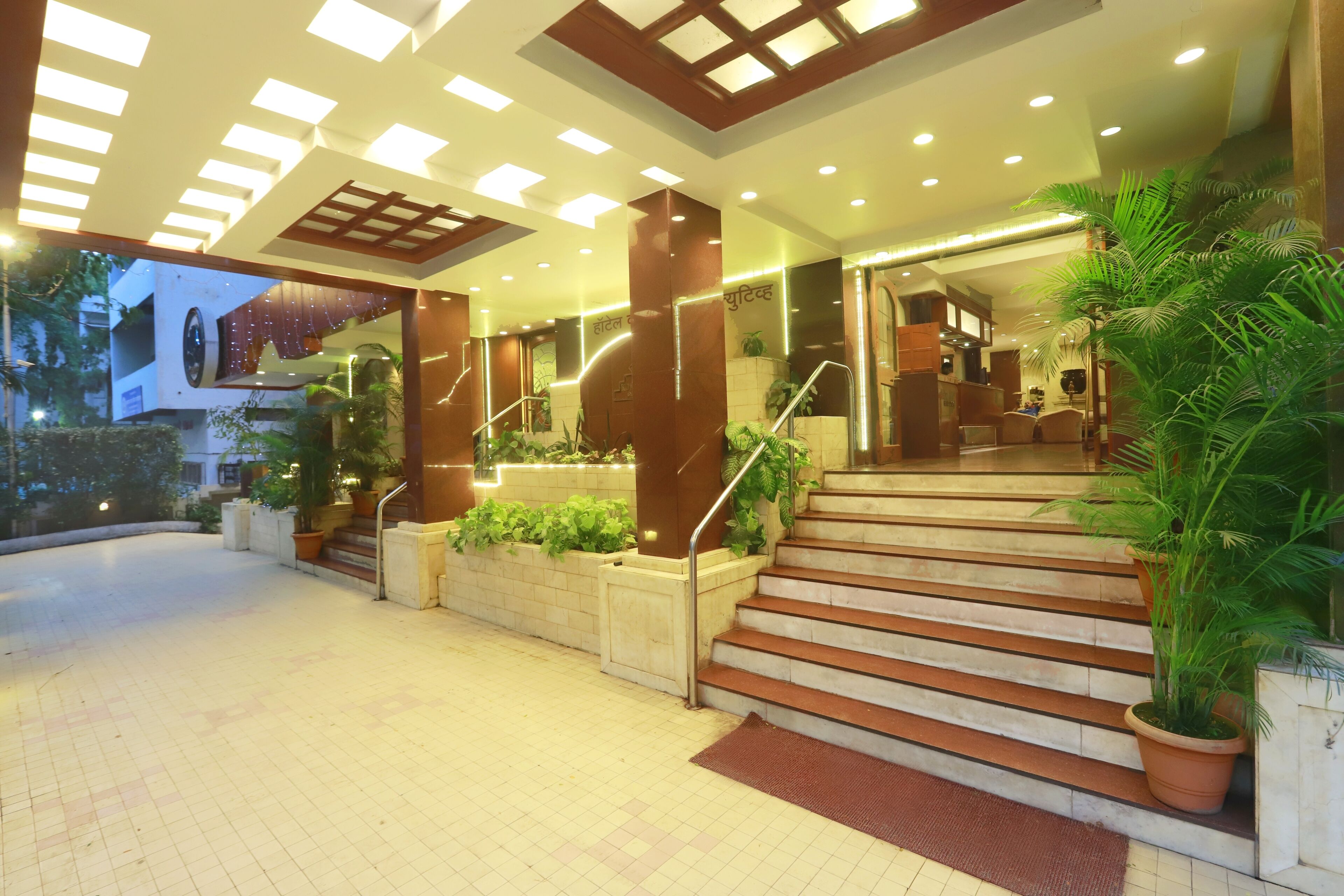 A hotel entrance with a staircase, potted plants, and a well-lit lobby area.