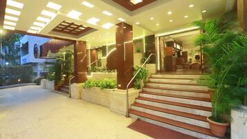 A hotel entrance with a staircase, potted plants, and a well-lit lobby area.