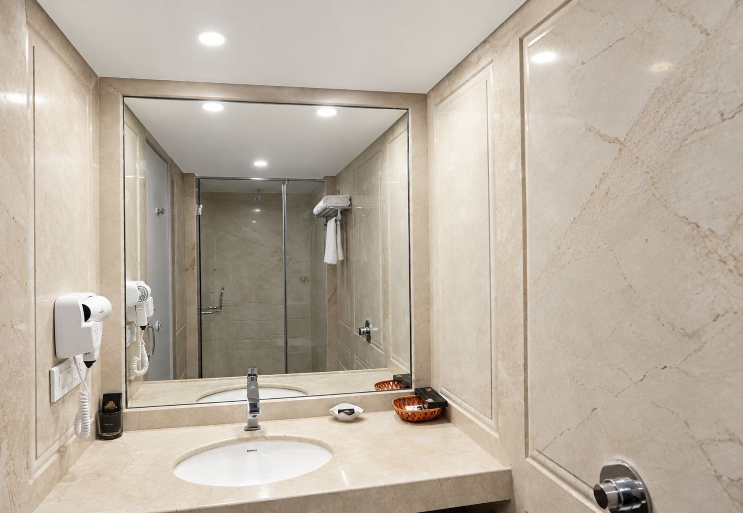 A bathroom with a large mirror, two sinks, a hairdryer, and a towel rack.