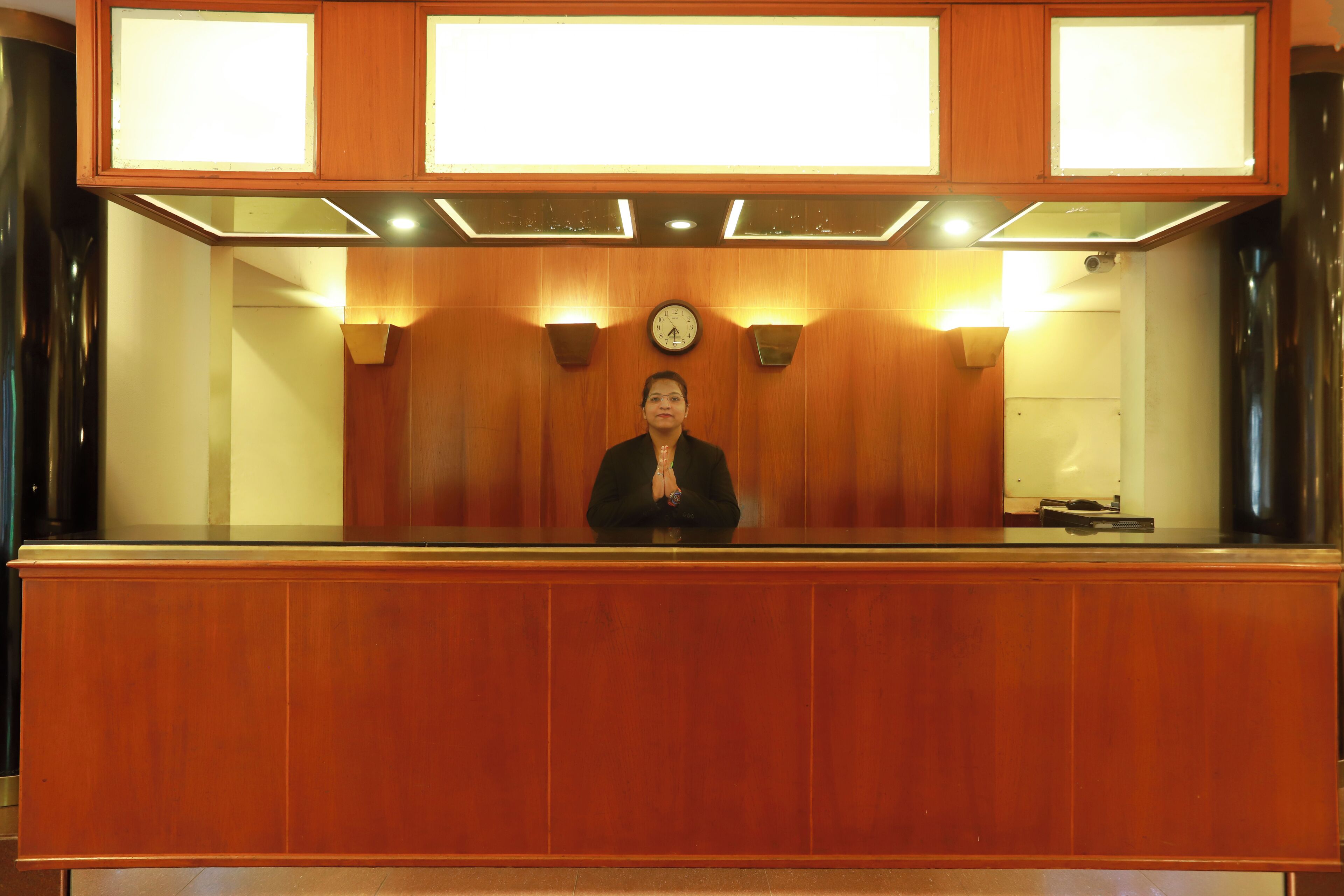 A reception desk with a clock, wooden paneling, and wall-mounted lights.