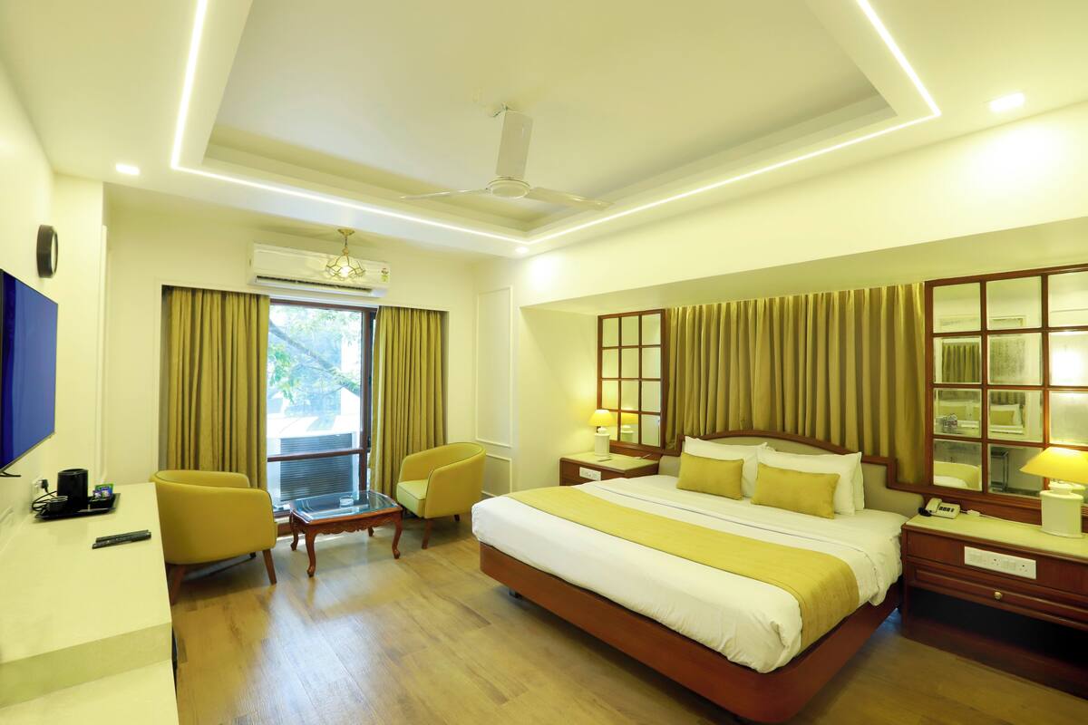 A hotel room with a large bed, a desk, a chair, a TV, and a window with curtains.