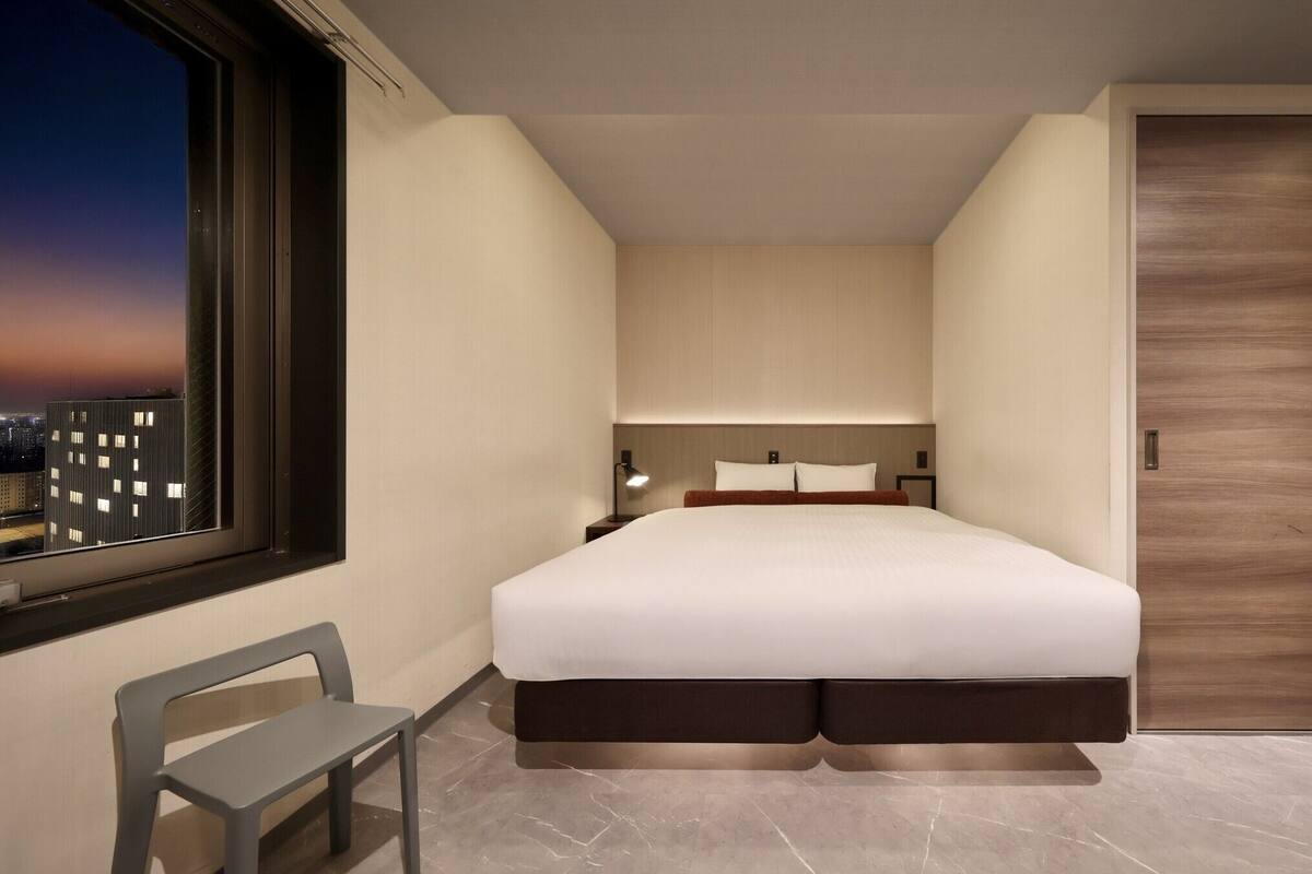 A modern hotel room with a large bed, a desk, and a chair.