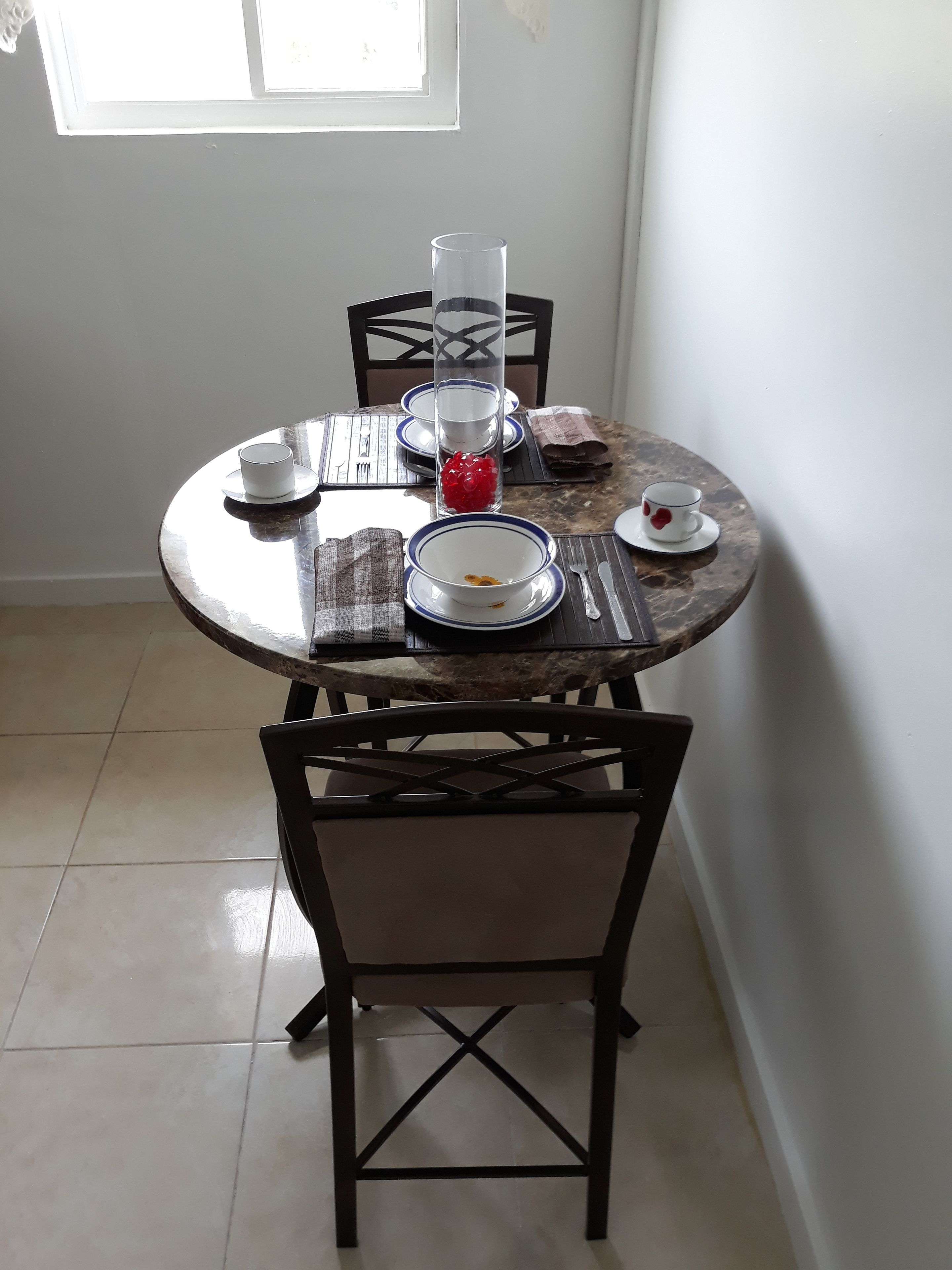A dining table with chairs, a glass vase with red flowers, and a white plate with a red heart design.