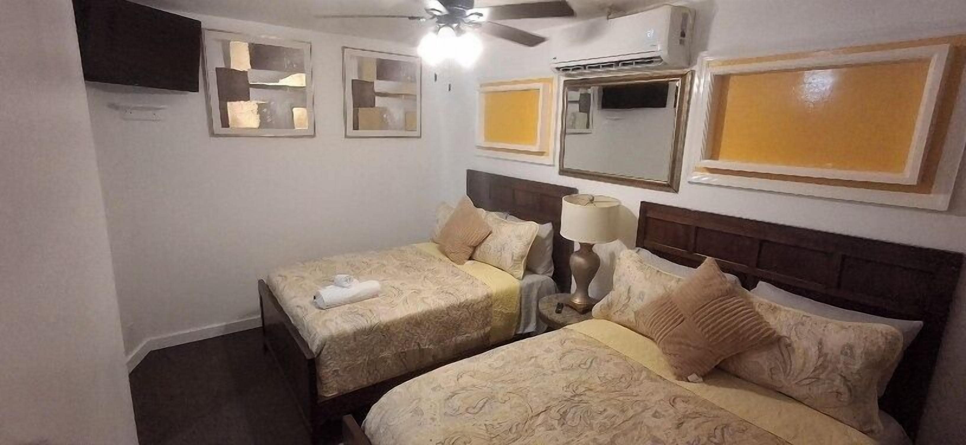 Ein Hotelzimmer mit zwei Betten, einem Deckenventilator, einer Klimaanlage und einem an der Wand befestigten Fernseher.