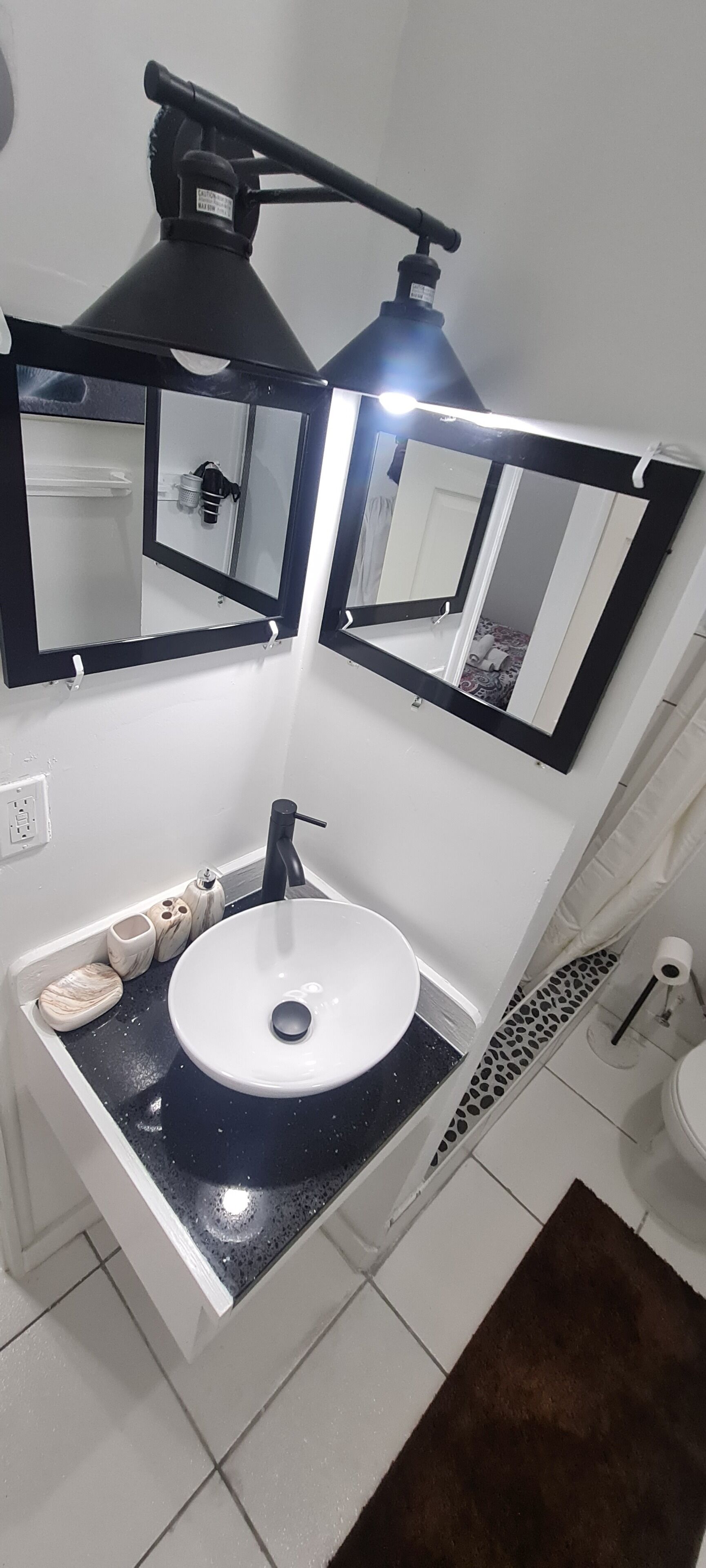 Un baño con lavamanos blanco, encimera negra y dos espejos.