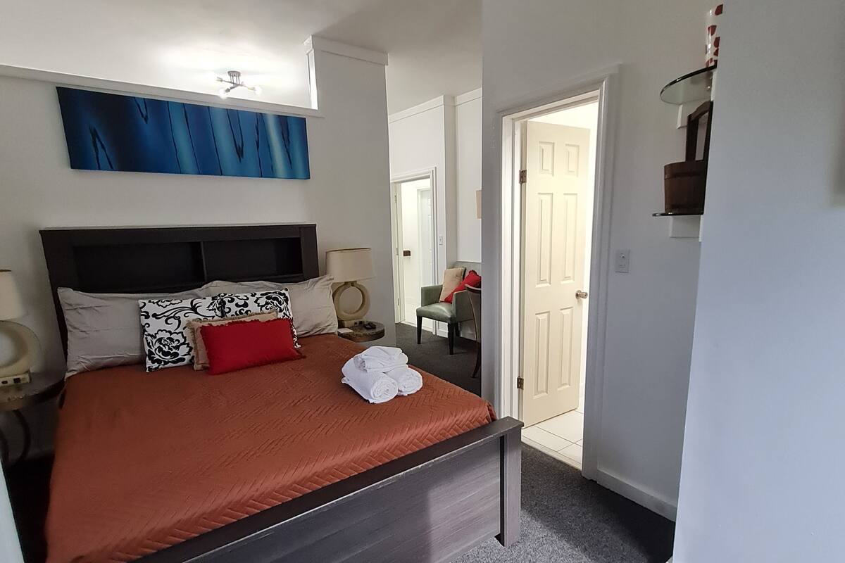 Un dormitorio con cama, ventilador de techo, un cuadro y una puerta que da a otra habitación.