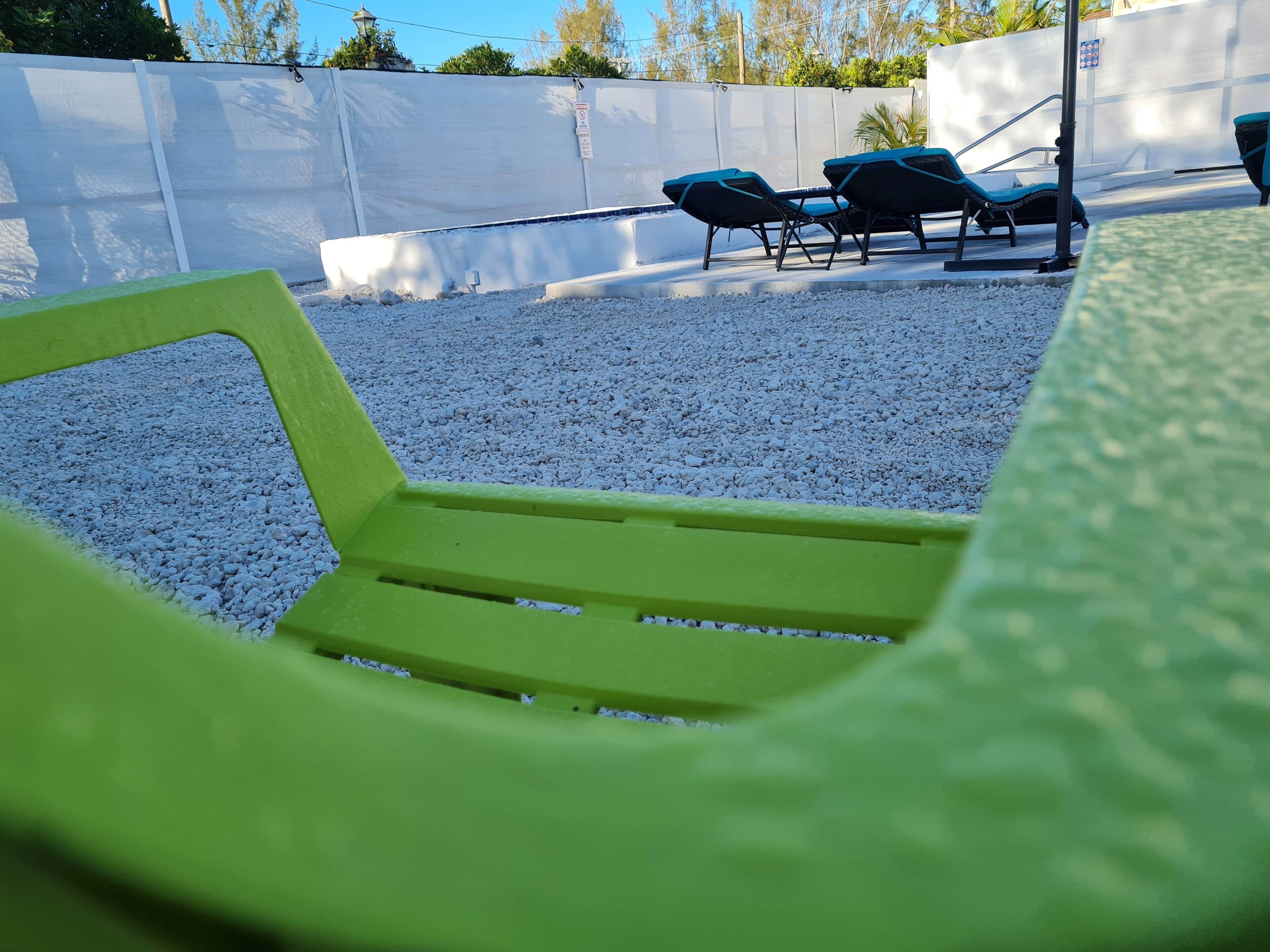 A patio area with a green chair, white gravel, and blue lounge chairs.