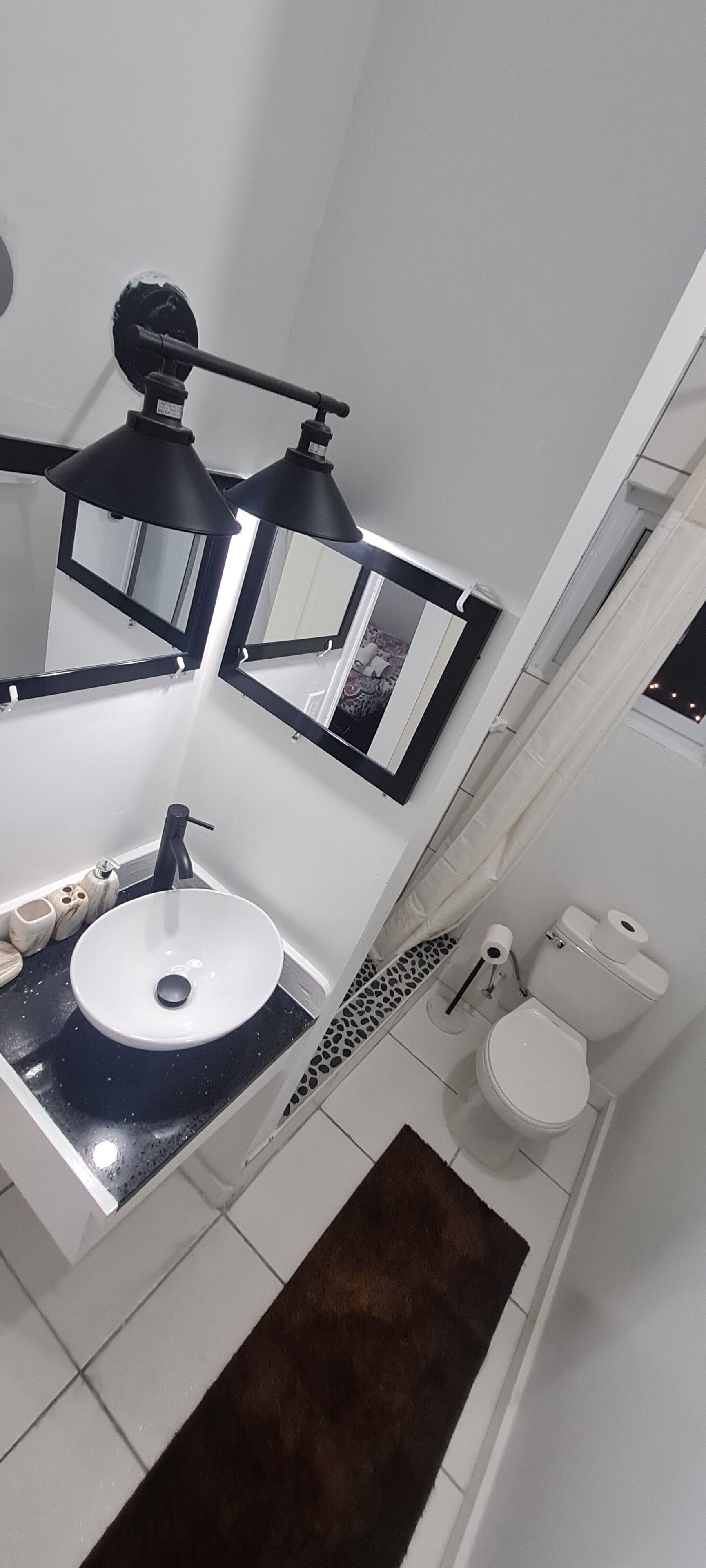 Une salle de bain avec un lavabo blanc, un plan de toilette noir et deux appliques murales noires.