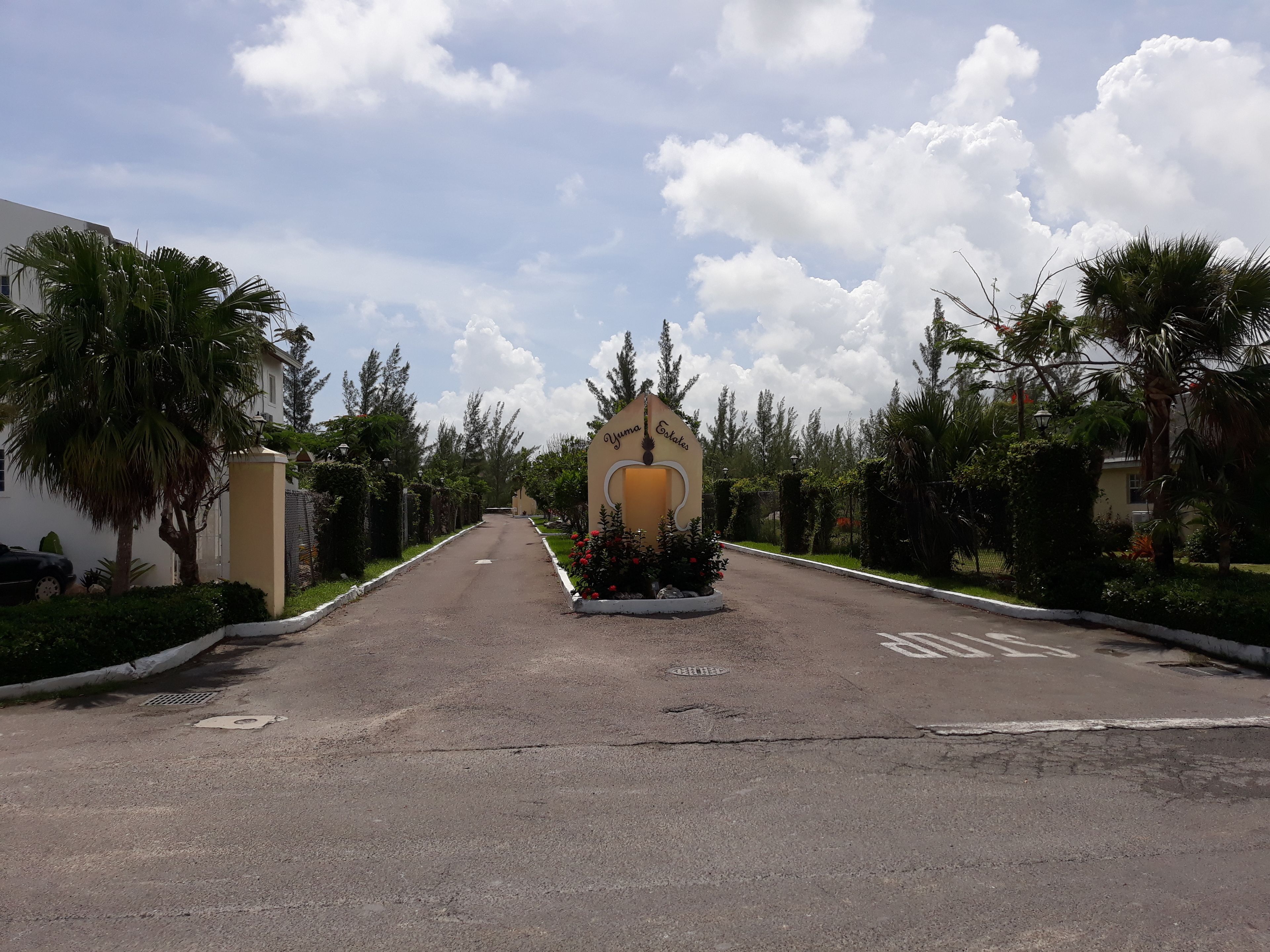 Una strada che conduce a un cancello con un cartello che riporta 'Yumo Estates'.