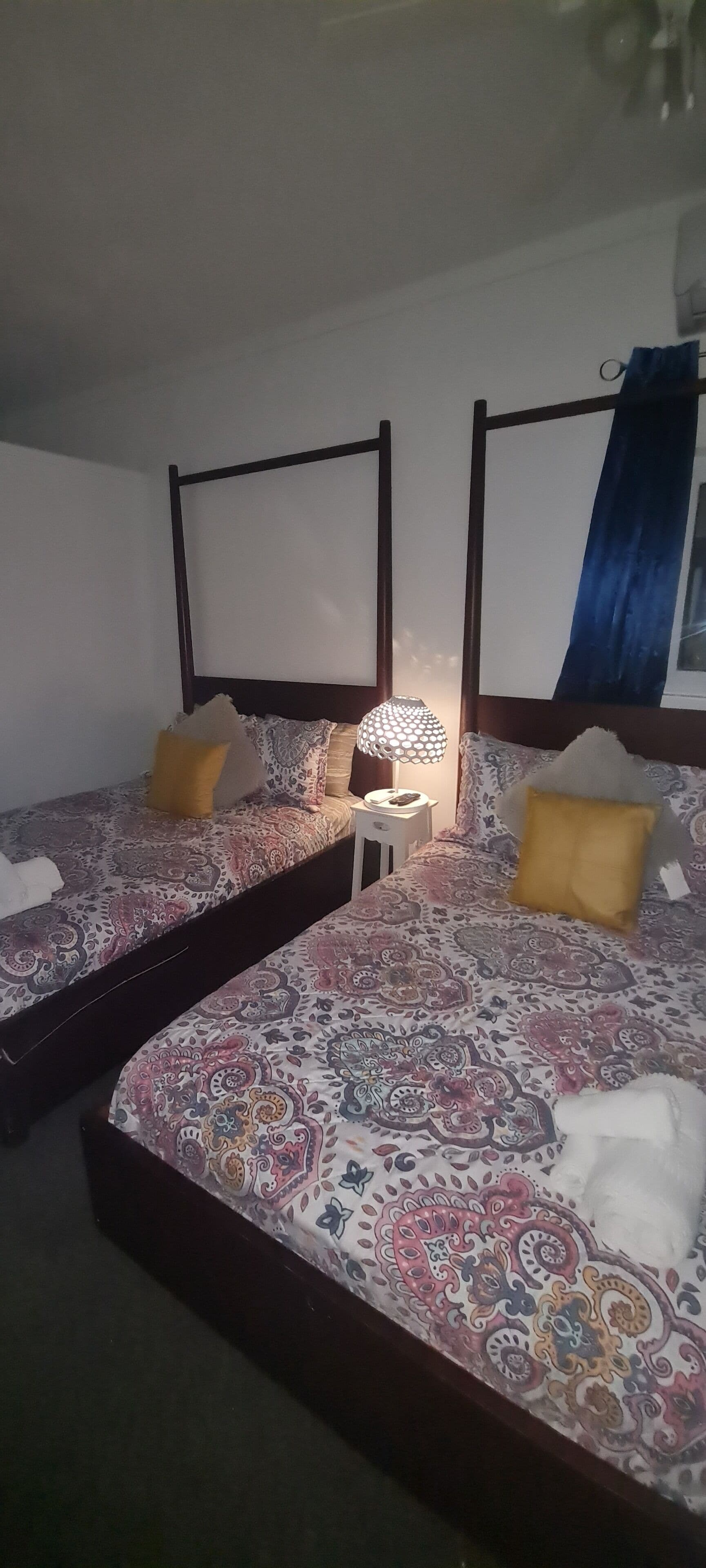 Ein Schlafzimmer mit zwei Betten, einem Nachttisch, einer Lampe und einem Fenster mit Vorhang.