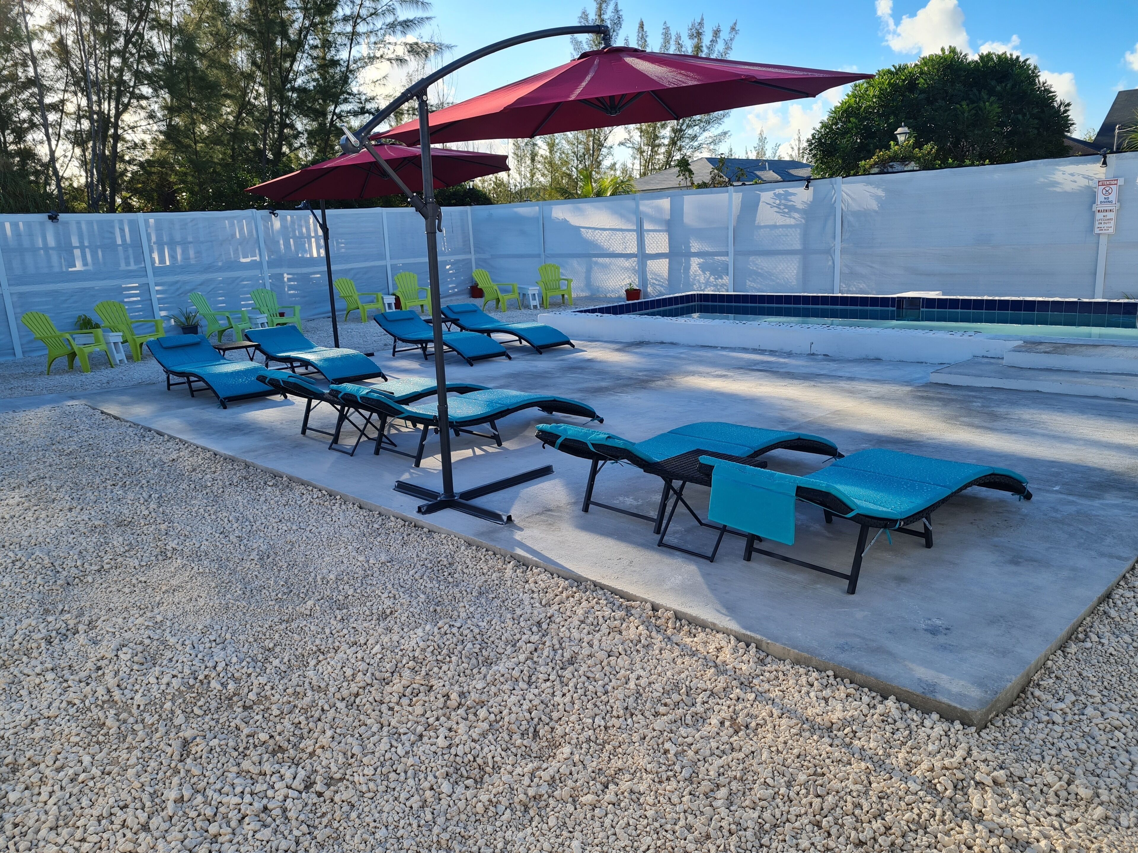 Un espace aménagé au bord de la piscine, avec des chaises longues et un parasol rouge.