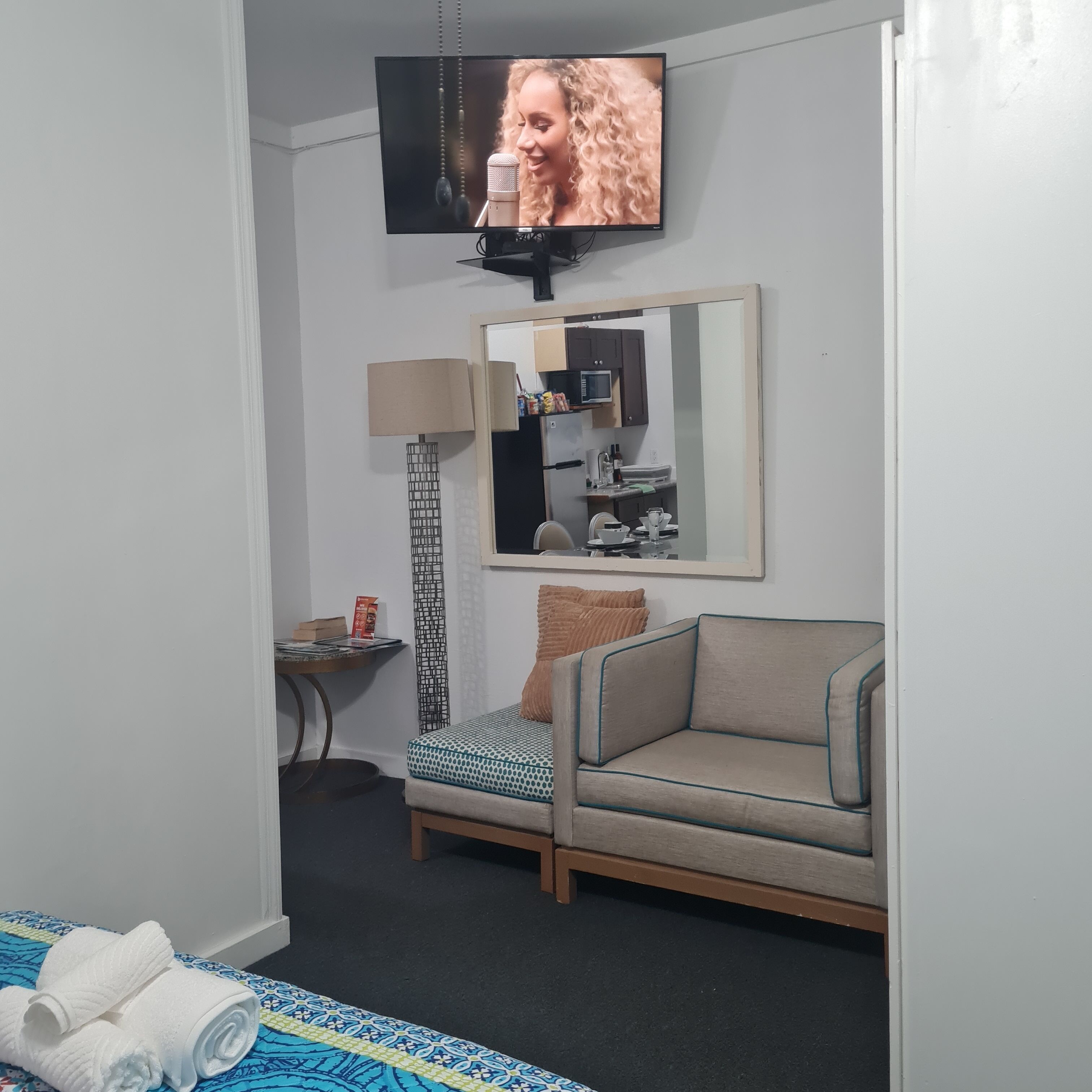 A hotel room with a sofa, a small table with a lamp, a television, and a mirror.