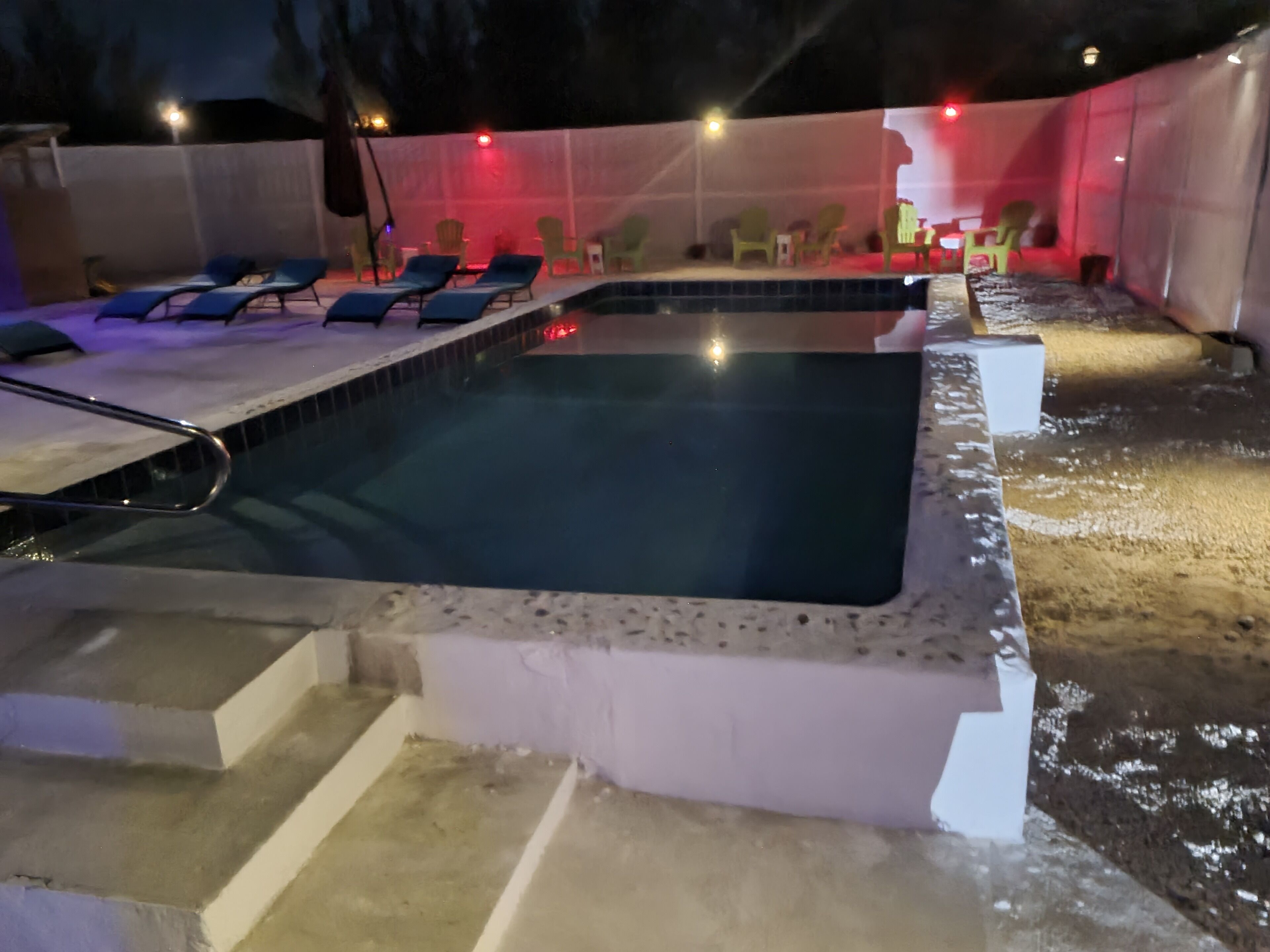 A swimming pool with lounge chairs and a covered area with chairs.
