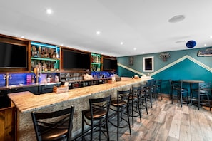 Una zona de bar con una barra larga, varios taburetes y estantes llenos de botellas.