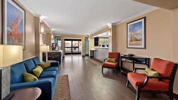 A spacious hotel lobby with a blue sofa, red armchair, and a small table. There is a kitchen area in the background.
